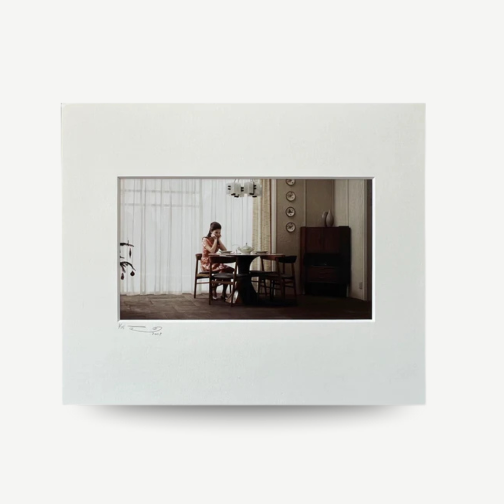 White digital photo frame displaying a photo of a woman sitting at a table. Erwin Olaf - Sarah from the 'Grief' series