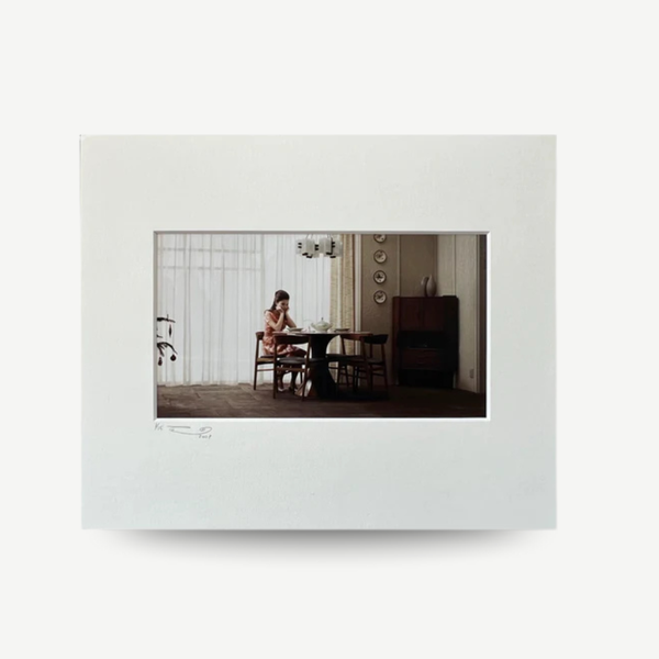 White digital photo frame displaying a photo of a woman sitting at a table. Erwin Olaf - Sarah from the 'Grief' series