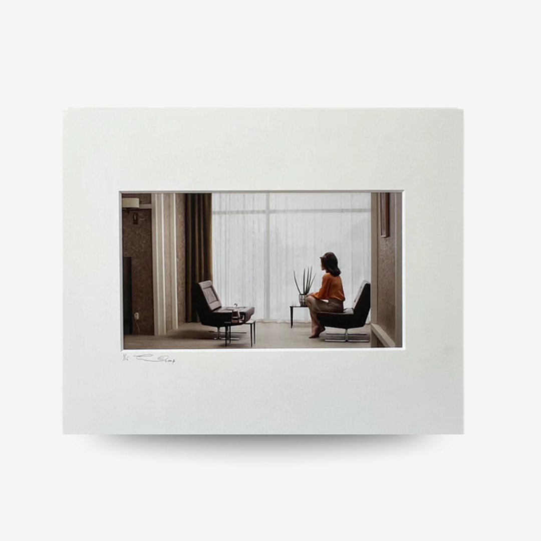 Framed photograph of a woman sitting in a modern room with large windows. Erwin Olaf - Caroline from the 'Grief' series