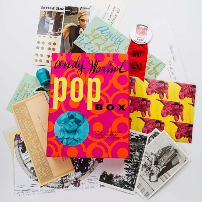 A collection of items related to Andy Warhol, including a 'Pop Box' book, postcards, prints, and other memorabilia spread out on a white surface.